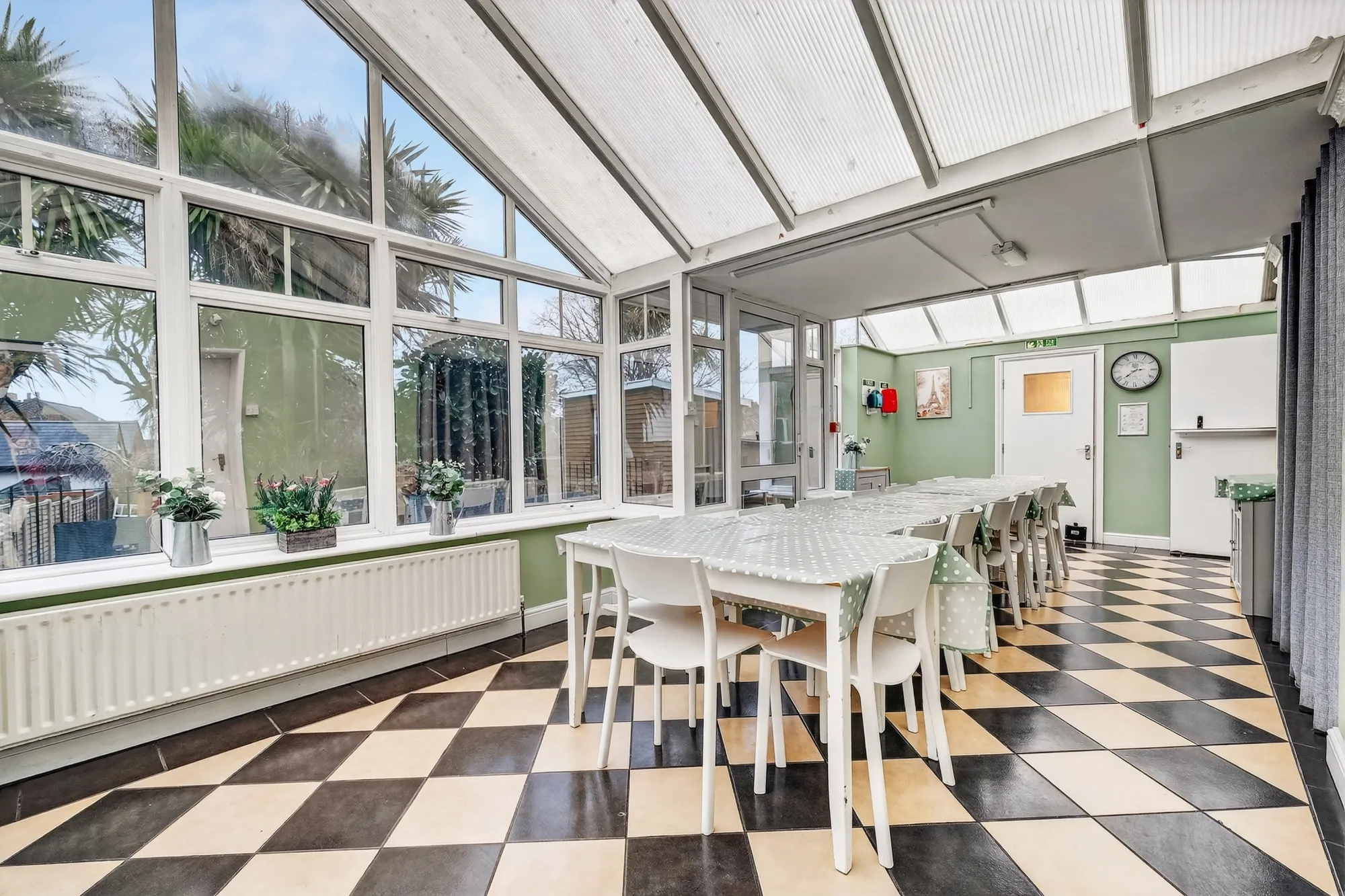 Bright conservatory dining area with communal tables and garden views at Pinfold Care Home