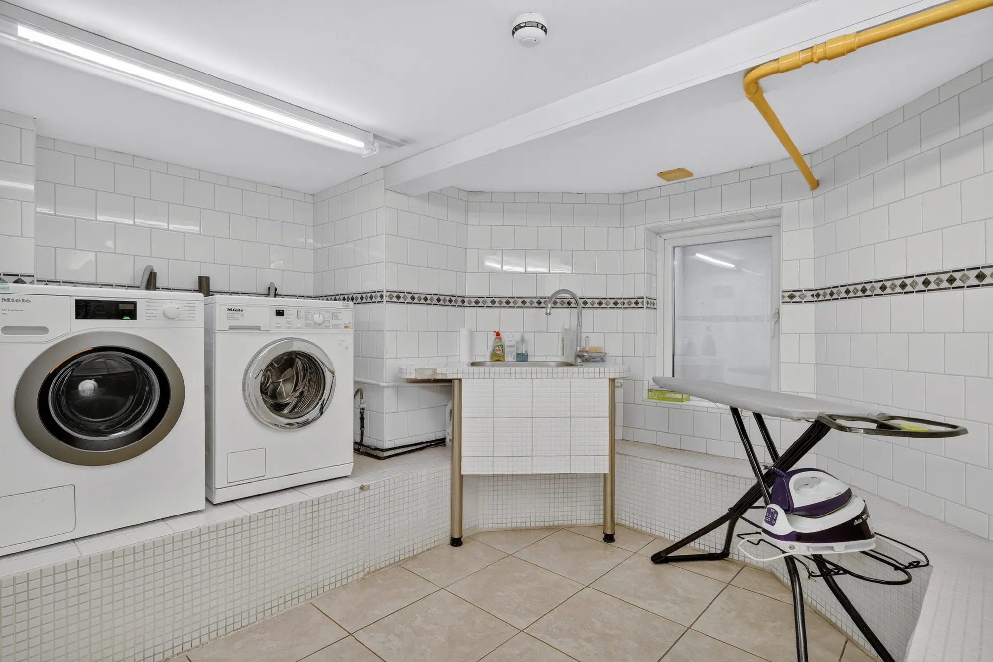 Clean and spacious laundry room with washing machines, dryers and ironing area at Pinfold Care Home
